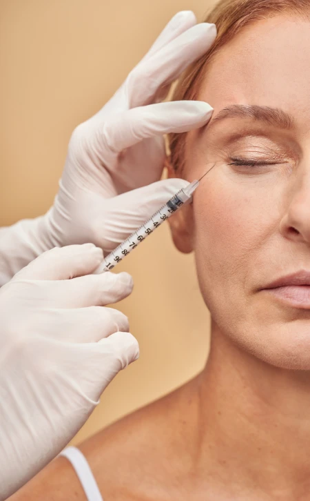 weibliches Gesicht bekommt eine Spritze seitlich neben dem Auge in die Haut gestochen