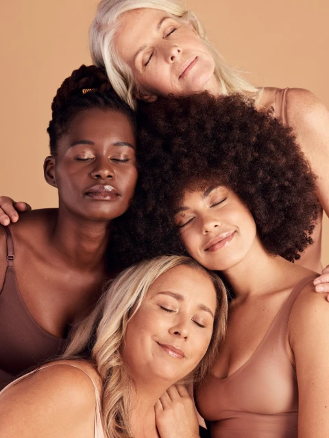 Home-Hero Vier Frauen unterschiedlicher Hauttöne und Altersgruppen eng aneinandergelehnt vor beigem Hintergrund