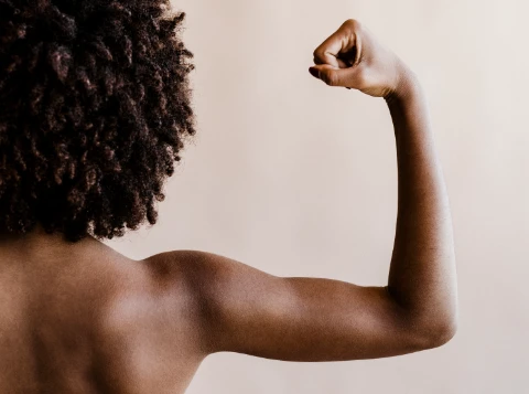 Frau mit Afro-Haaren zeigt ihren angewinkelten Arm in kraftvoller Pose